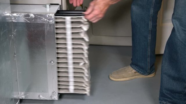 Static 4K shot of a senior man changing a large air filter from HVAC furnace system