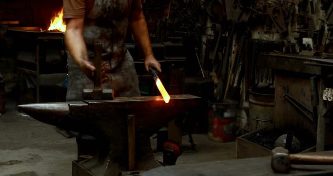Blacksmith examining a hot metal rod with brush 4k