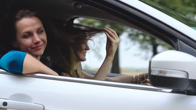 Two young women ride in a car and have fun. Slow motion
