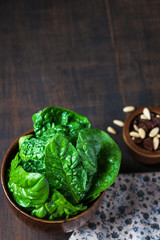 Fresh spinach with raisins, pinions in a wooden bowl on rustic wooden background, selective focus. Vertical. Spase for text.