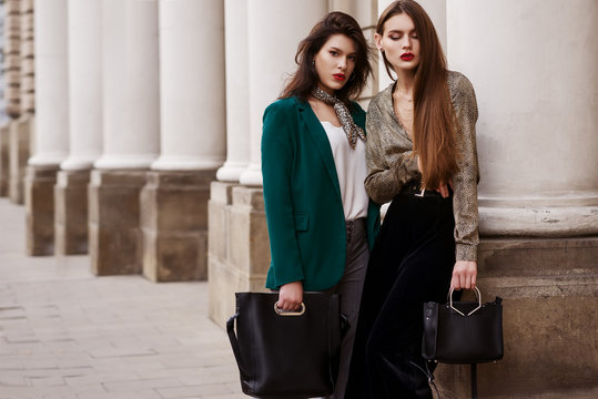 Outdoor fashion portrait of two young beautiful women wearing trendy clothes, accessories with animal print, holding black leather bags, posing in street of european city. Copy, empty space for text