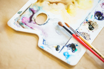 Palette with watercolors in different colors. Various brushes and pencils for drawing prepared by the artist for work.