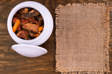 Meat goulash with carrots, zucchini and tomatoes, stewed with ceramic pot, next to a wooden...