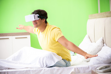 Fototapeta na wymiar Young man with virtual glasses in the bedroom 
