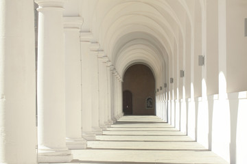 A bright corridor of many columns in a medieval castle. Selective focus on light and shadows from classical columns in the old building of Europe. The entrance is at the end of the tunnel.