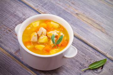 Chicken, butternut squash, apple, ginger and sage stew in white bowl on wooden table. Pumpkin soup with chicken. horizontal