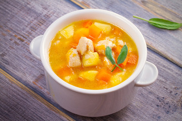 Chicken, butternut squash, apple, ginger and sage stew in white bowl on wooden table. Pumpkin soup with chicken. horizontal