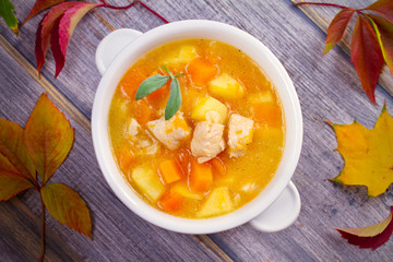 Chicken, butternut squash, apple, ginger and sage stew in white bowl on wooden table. Pumpkin soup with chicken. overhead, horizontal