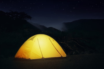 Illuminated Camping Tent at Night Under Starry Sky in the Forest with Mountain View - Travel Destination Inspiration Concept