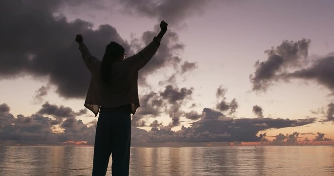 Silhouette of woman raising hand at sunrise time