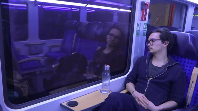 A wide shot of a young man watching outside towards the passing landscape, sitting in a german train.