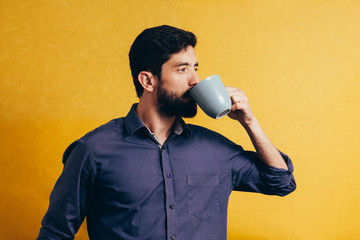 Portrait of handsome man drinking coffee over yellow background