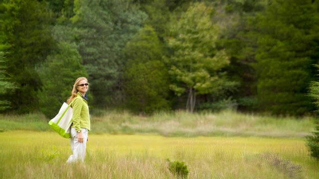 Cinemagraph of a pretty woman walking in a grassland meadow set against a mature forest.