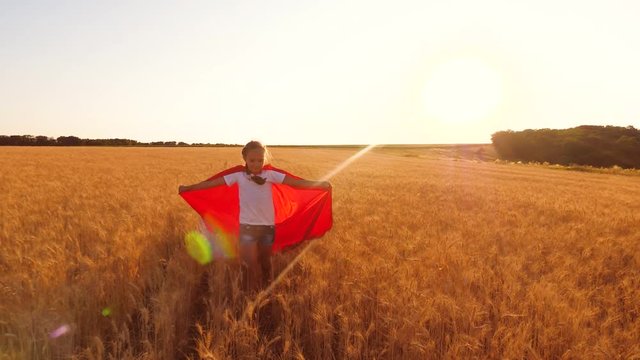 superhero young girl in red raincoat playing on field of ripe wheat, girl runs against sunset