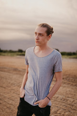 Attractive Young Male Model with Man Bun and Long Blonde Hair Posing for Camera Outside in Filed During Sunset