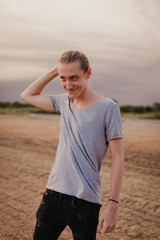 Attractive Young Male Model with Man Bun and Long Blonde Hair Posing for Camera Outside in Filed During Sunset