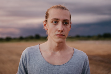 Attractive Young Male Model with Man Bun and Long Blonde Hair Posing for Camera Outside in Filed During Sunset