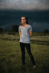 Obraz premium Attractive Young Male Model with Man Bun and Long Blonde Hair Posing for Camera Outside in Filed During Sunset