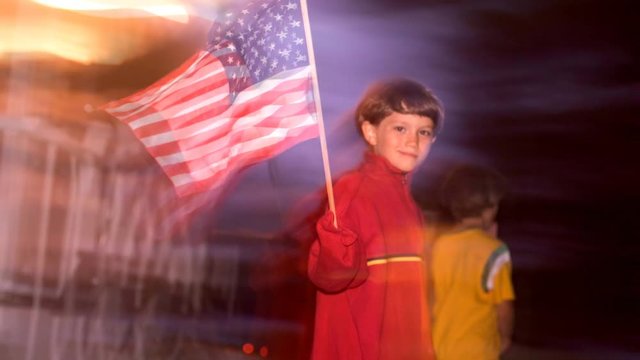 Cinemagraph of a small boy waving an american flag with background motion.