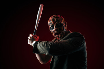 scary halloween theme and halloween makeup: scary man with a burnt face holds a baseball bat in his...