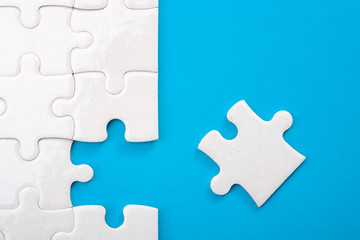Teamwork, completing the final task and finding the solution concept with the missing piece of a jigsaw puzzle next to unfinished board isolated on blue with copy space