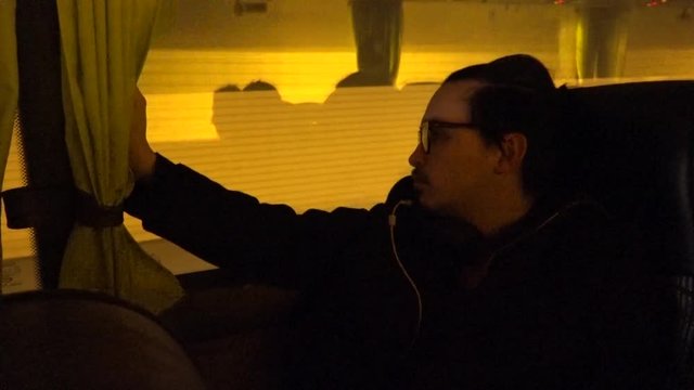 A tired young man with headphones looking out of a bus, a Flixbus, while it rides through a tunnel.