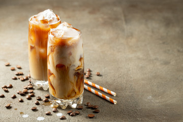 Ice coffee in a tall glass with cream poured over and coffee beans. Cold summer drink on a brown rusty background with copy space