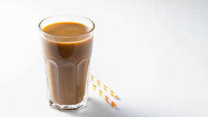 Ice coffee in a tall glass with cream poured over and coffee beans. Cold summer drink on white background with copy space