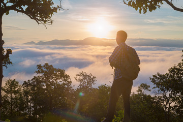 Tourist with backpack on  mountain slope with raised hands over, The valley is covered with  fog and has a beautiful sunrise. Beauty of nature, tourism and traveling concept.