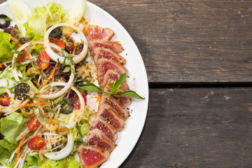 Close up of rare seared tuna slices with fresh vegetable salad on a plate with wood background