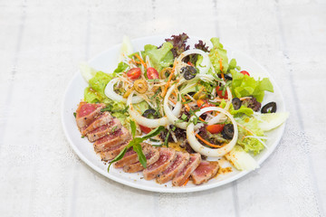 Close up of rare seared tuna slices with fresh vegetable salad on a plate with wood background