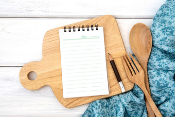 a  lined book notepad paper on chopping cutting board and tablecloth with wooden fork and spoon on...