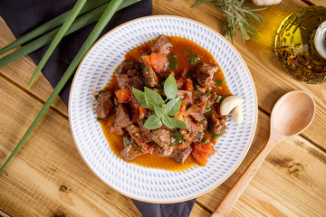 stewed beef on a wooden table with greens and potatoes