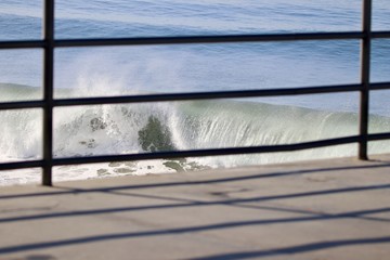 waves crashing viewed through hand rails on a pier
