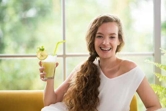 Healthy young woman lying on a couch holding a glass of fruit juice looking relaxed and comfortable