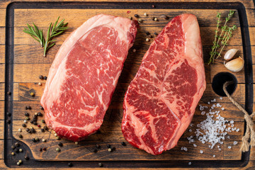 Fresh raw Prime Black Angus beef steaks with spices on wooden board: Striploin, Rib Eye. Top view....