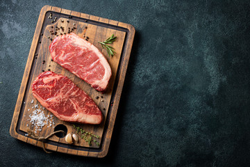 Fresh raw Prime Black Angus beef steaks with spices on wooden board: Striploin, Rib Eye. Top view...