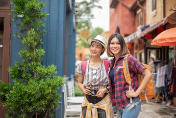 Young Asian women backpacks have fun with shopping  and happy are taking photo at outdoor mall/supermarket/market in the evening; Attractive young woman spend time together.