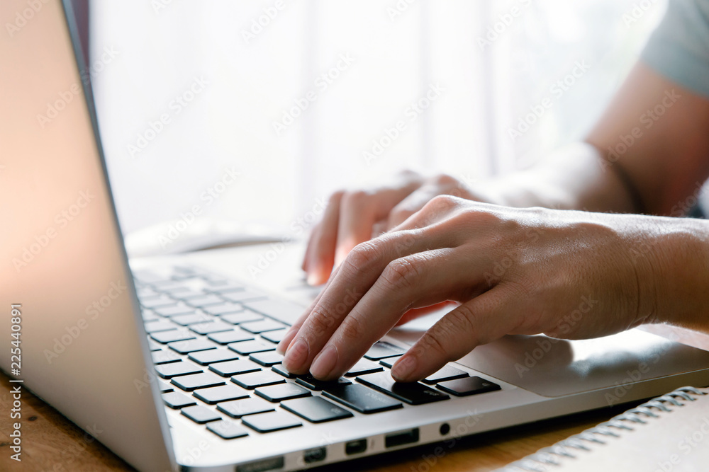 Poster closeup image of hands working and typing on laptop keyboard in front of the window in soft light