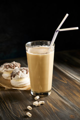 Iced coffee in tall glasses with milk and straws on board over rustic wooden table, white wall and jug at background, copy space. Summer refreshing beverage ice coffee drink concept