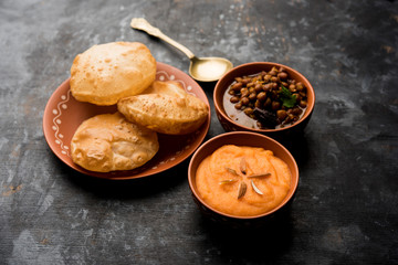 Suji/Sooji Halwa Puri or Shira Poori with black chana masala breakfast, served in a plate and bowl. selective focus