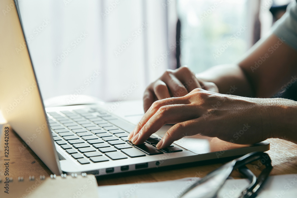 Poster man working at home office using a laptop computer on wooden table. hands typing on a keyboard.