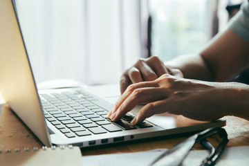 Man working at home office using a laptop computer on wooden table. Hands typing on a keyboard.
