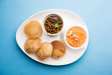 Suji/Sooji Halwa Puri or Shira Poori with black chana masala breakfast, served in a plate and bowl. selective focus