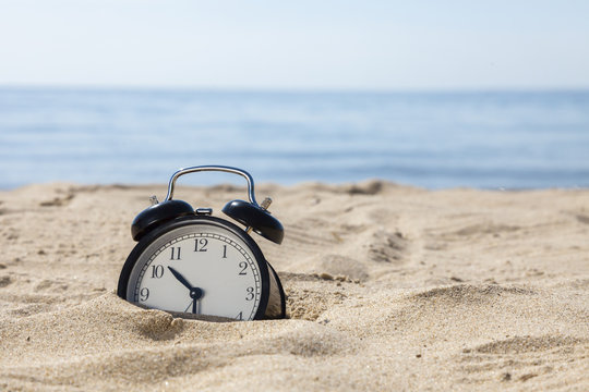 Time to relax! The alarm clock on the sand shore of the sea.