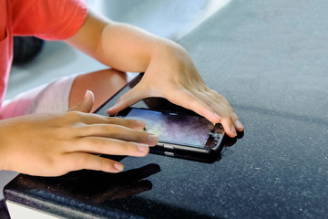 The boy plays in the phone on a black table with a shiny surface