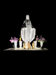 Statue of the Virgin Mary with candles on a black background