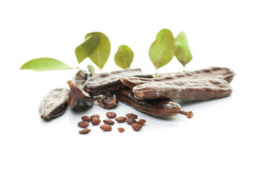 Carob bean on white. Healthy organic sweet carob pods with seeds and leaves, healthy eating and food background.
