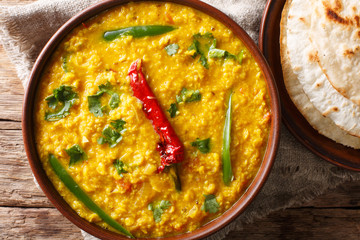 Lentil soup Dal Tadka with naan bread in a ceramic bowl on a wooden background. horizontal top view