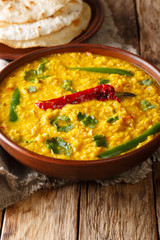 Dal Tadka yellow lentil Indian soup with flat bread on a wooden table close-up. Vertical